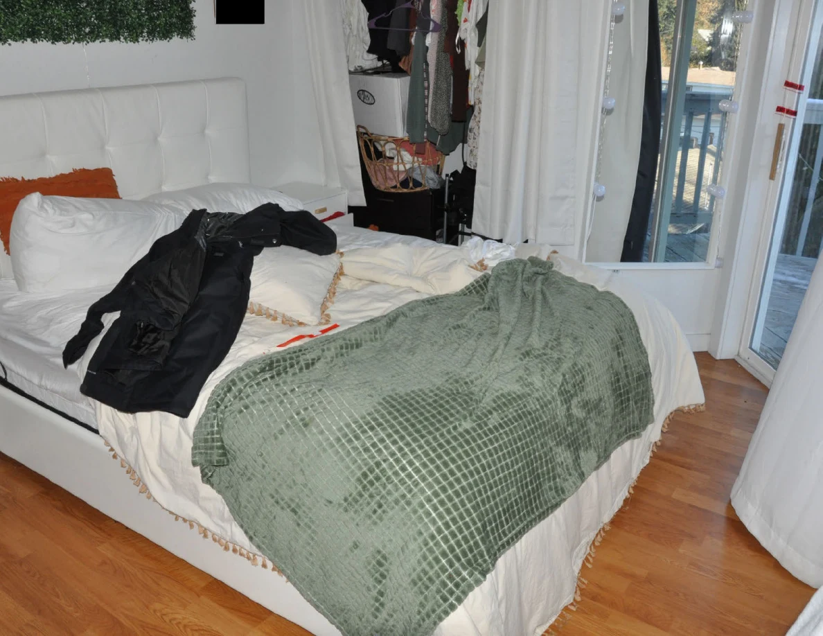 White bed with green blanket and dark garment beside a mirrored panel and balcony doorway.
