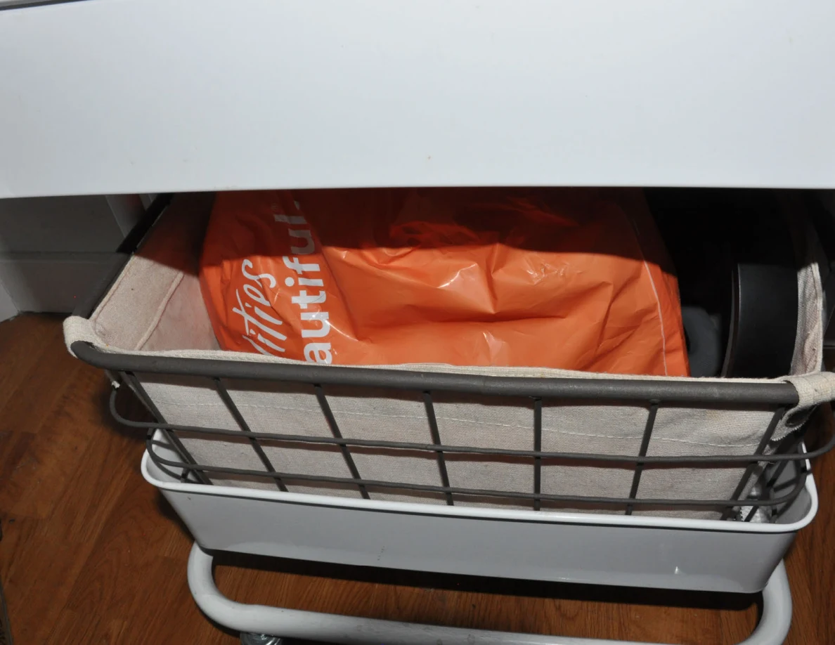 Fabric basket with an orange shopping bag on the bottom of a wire-framed cart.