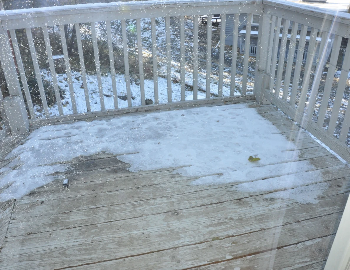 Weathered balcony deck with patchy snow behind a white railing.