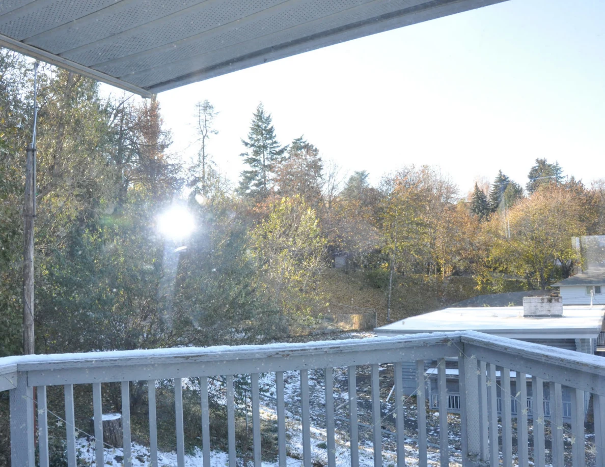 View from a balcony beneath a roof overhang toward autumn trees and nearby rooftops.