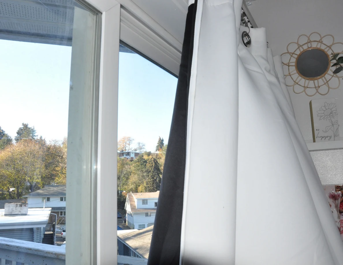 Upper glass balcony doorway and white curtain beside a small round wall mirror.
