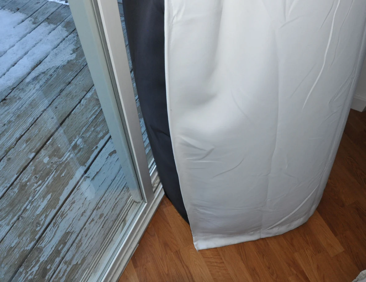 Bottom of a white curtain at a balcony threshold above wood-pattern indoor flooring.