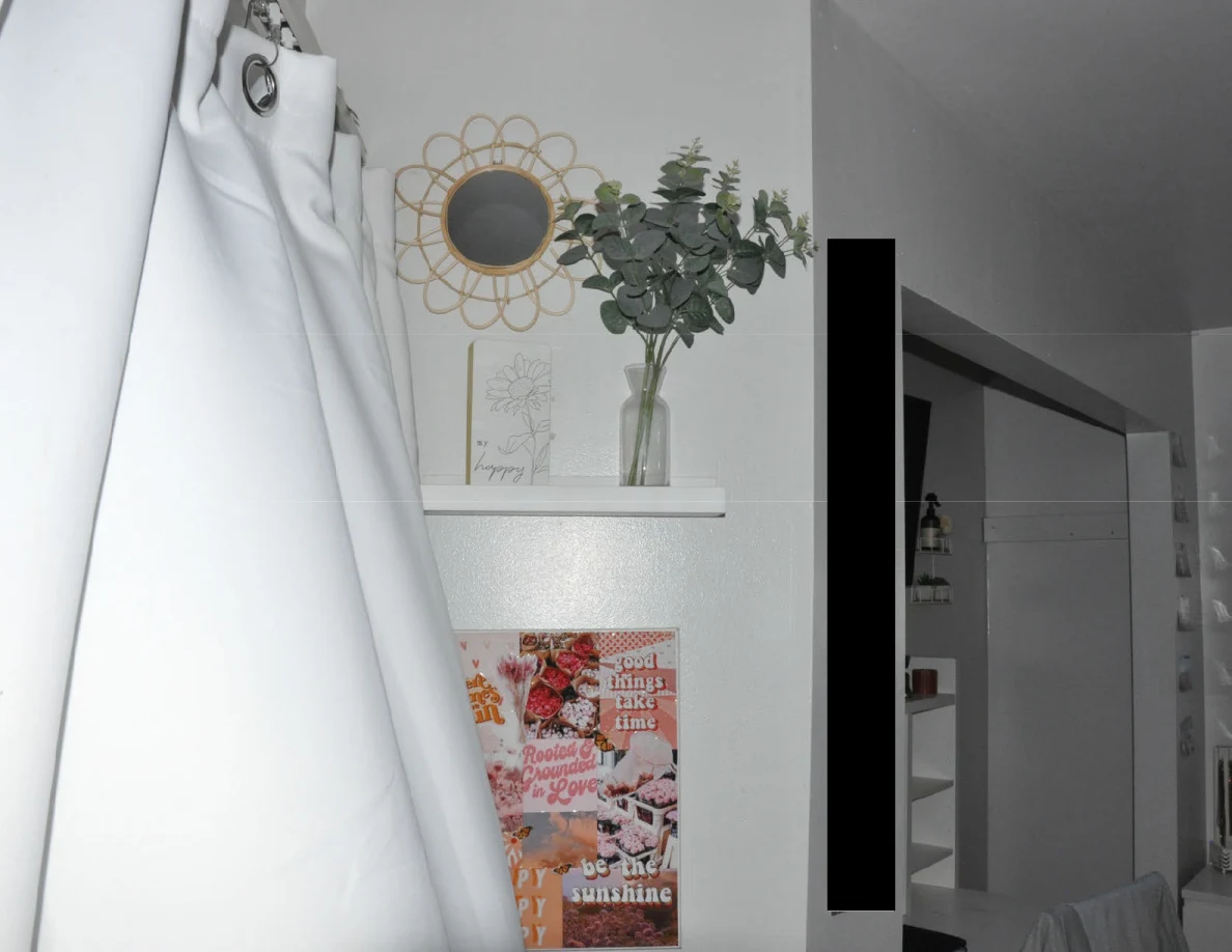 Small wall shelf with vase and leafy stems beside a round decorative mirror and curtain.