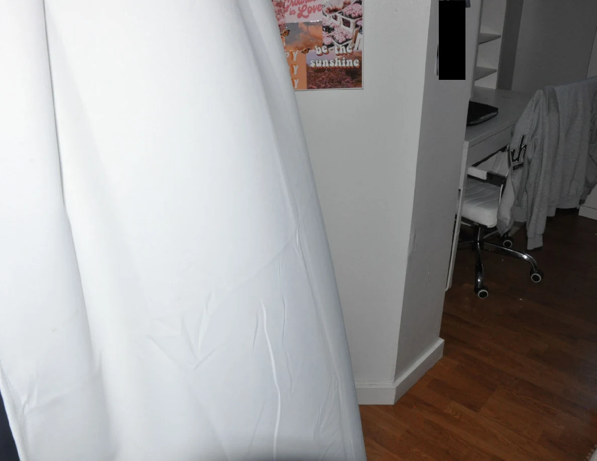 White curtain beside a colorful wall collage and vanity area.