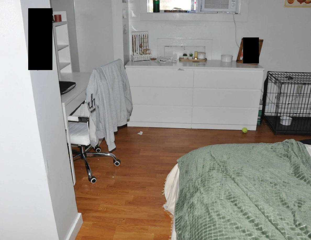 View across a bed toward a dresser, chair and pet crate.