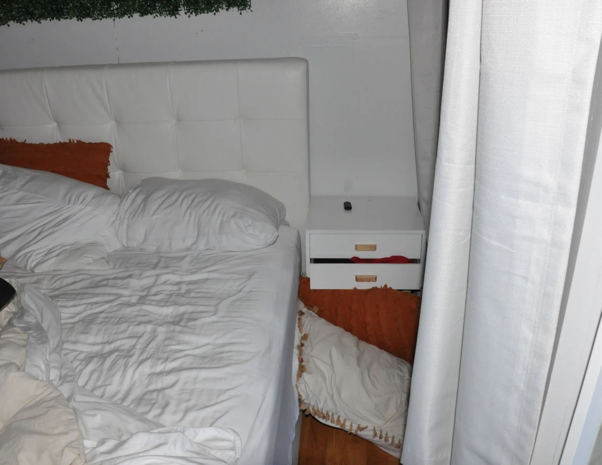 White bed and bedside drawers beside curtains, with pillows on the floor.