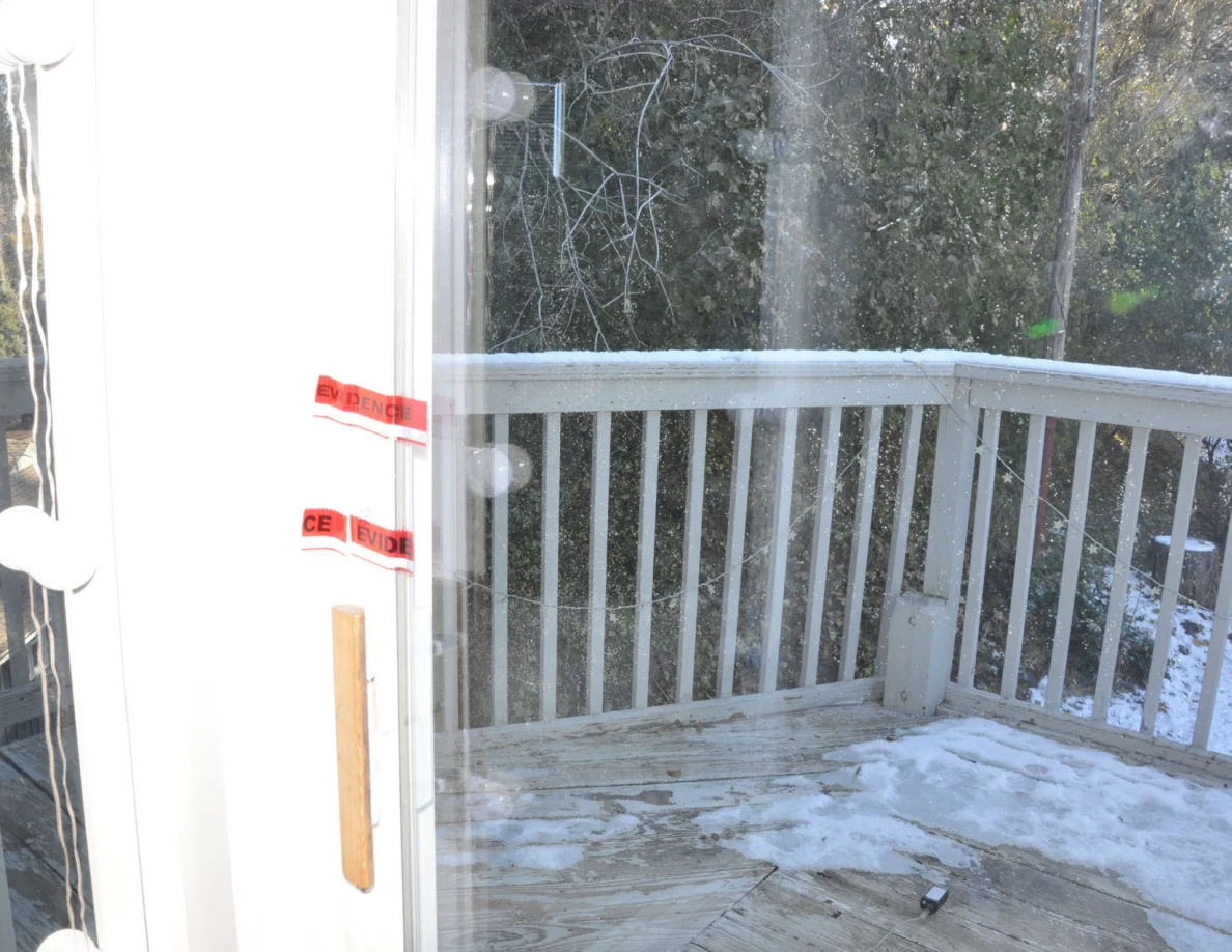 Red evidence tape across a balcony door frame beside a snow-dusted deck and railing.