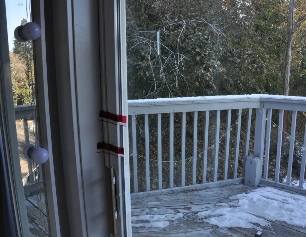 Balcony doorway with red tape beside an illuminated mirror and snowy railing.