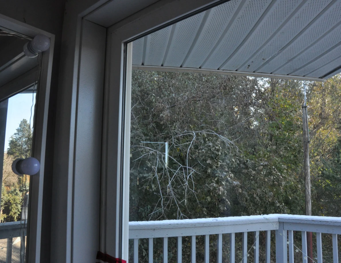Upper glass door frame and roof overhang with trees beyond the balcony.