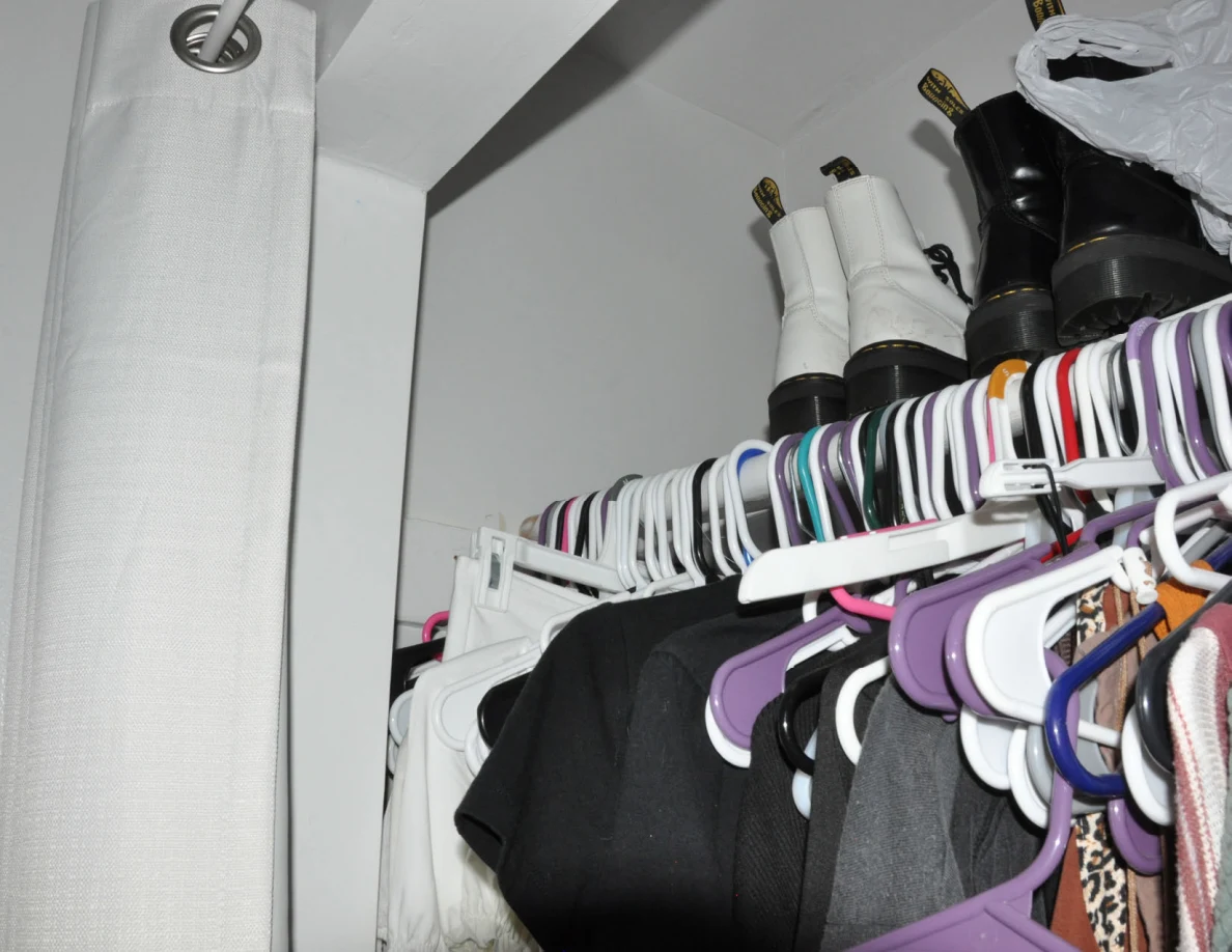 Closet rail crowded with hangers beneath boots on an upper shelf.