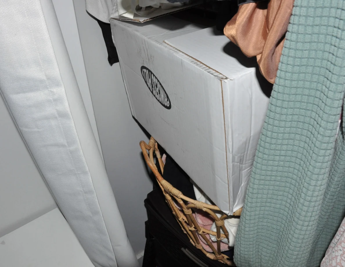 Large white storage box beneath hanging clothes beside a curtain.