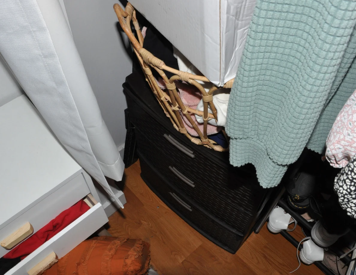 Basket and black drawer unit beneath hanging clothes beside bedside drawers.