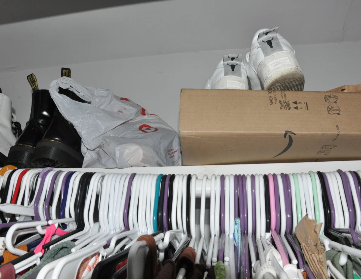 Shoes and a cardboard shipping box on a closet shelf above hangers.