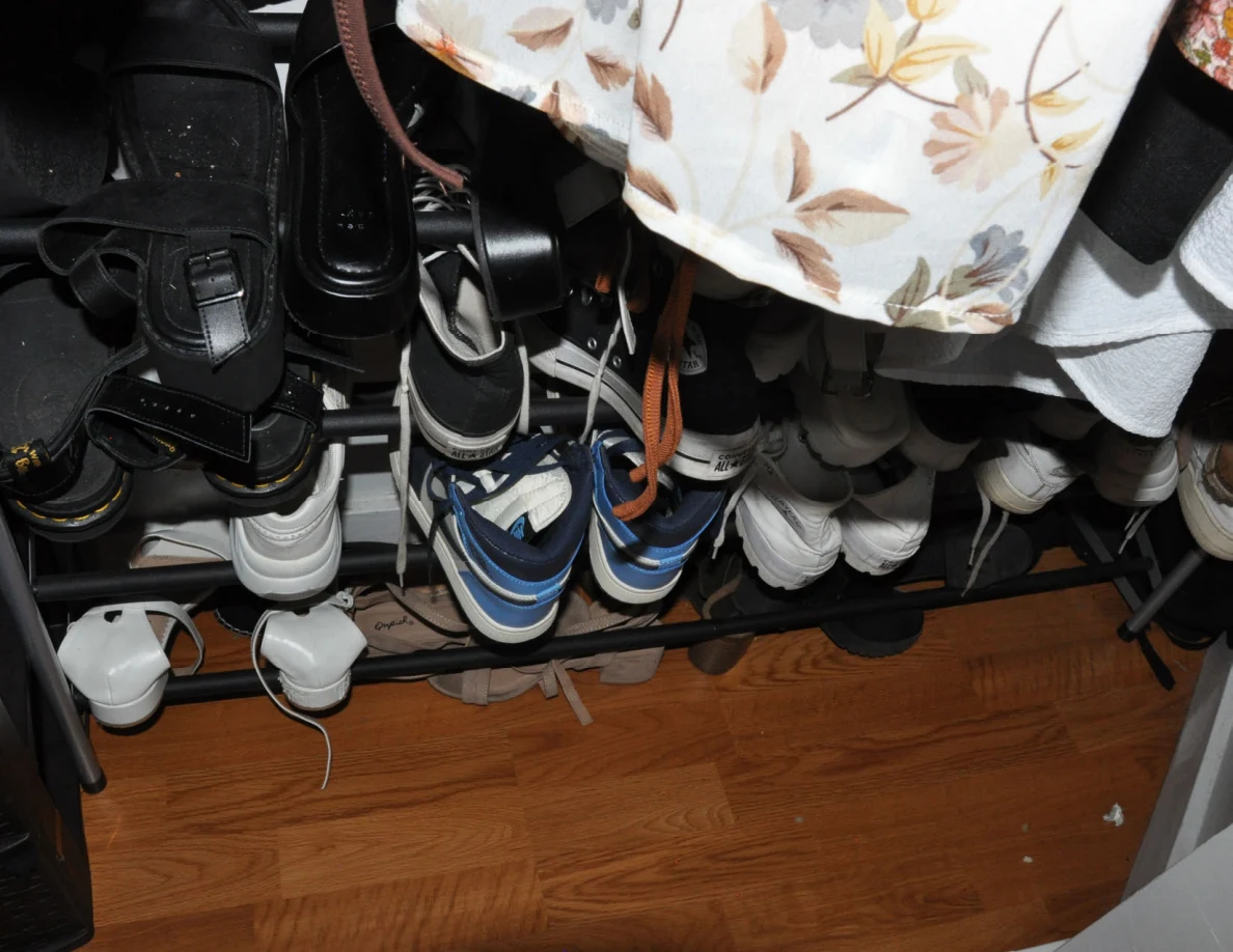 Shoe rack filled with footwear beneath hanging clothes.