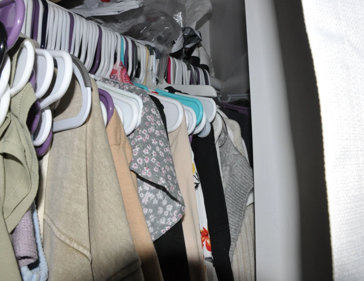 Close angled view of garments on hangers beside a closet curtain.