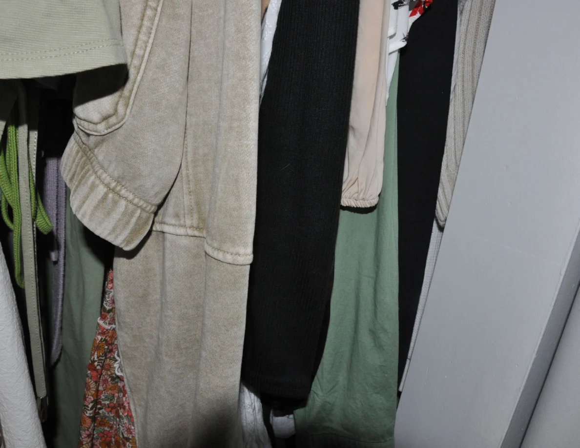 Lower hanging gray, black and green garments inside a closet.