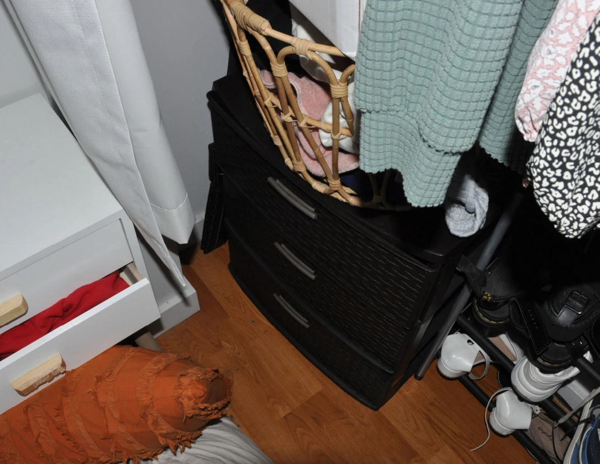 Black woven-look drawer unit beneath a basket and hanging clothes.