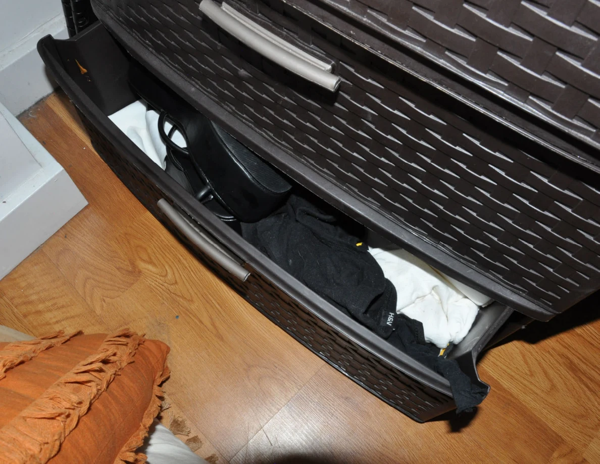 Open lower black drawer containing folded and loose clothing.