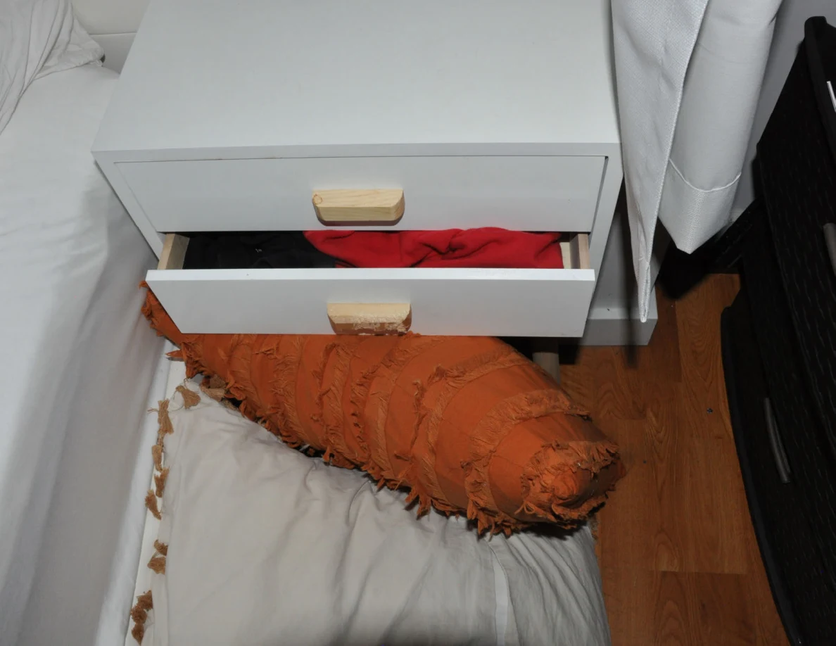 White bedside drawers with red fabric visible and pillows on the floor.