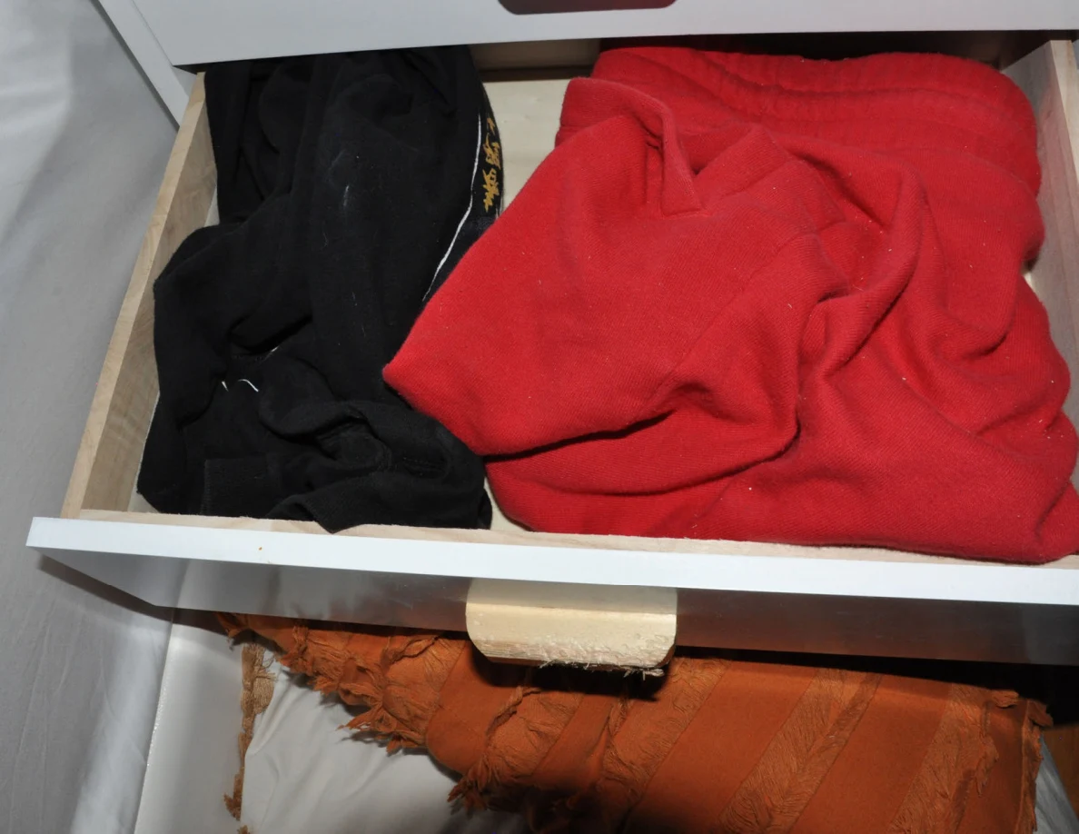Close view of an open bedside drawer containing red and black clothing.