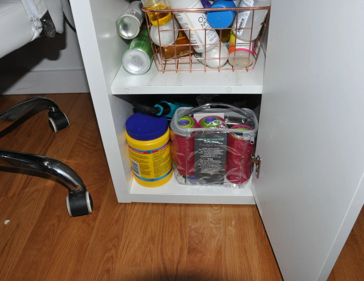 Open vanity cupboard with bottles, cans, wipes and a clear toiletry bag.