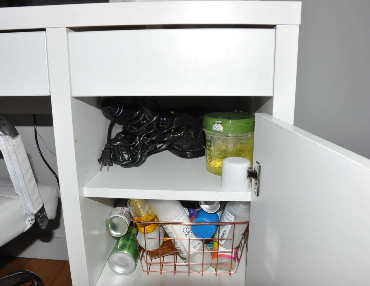 Closer view of open cupboard shelves with cords, containers and toiletries.