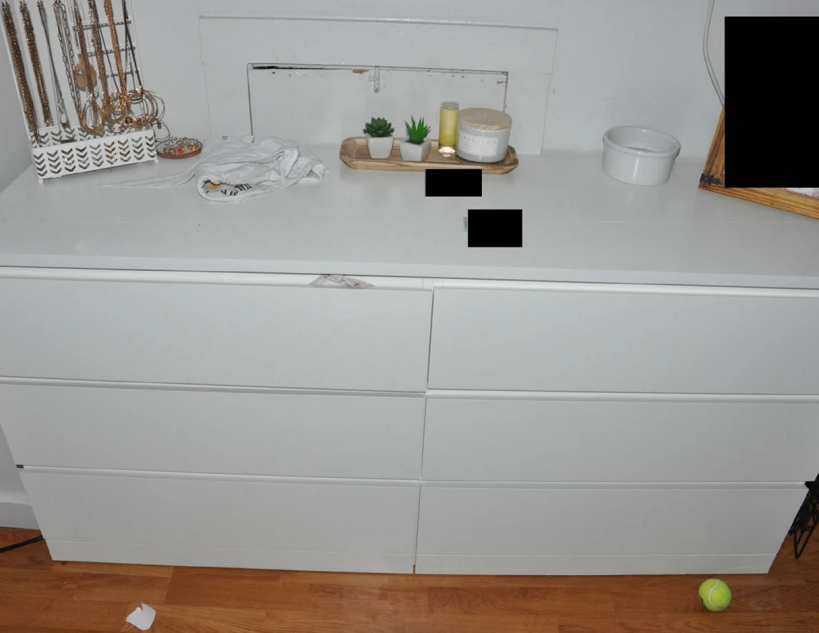 White dresser with jewelry organizer, small plants, candles and redacted items on top.