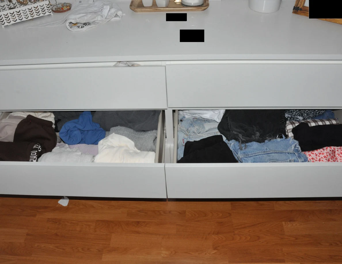 Open dresser drawers containing folded shirts, jeans and dark garments.