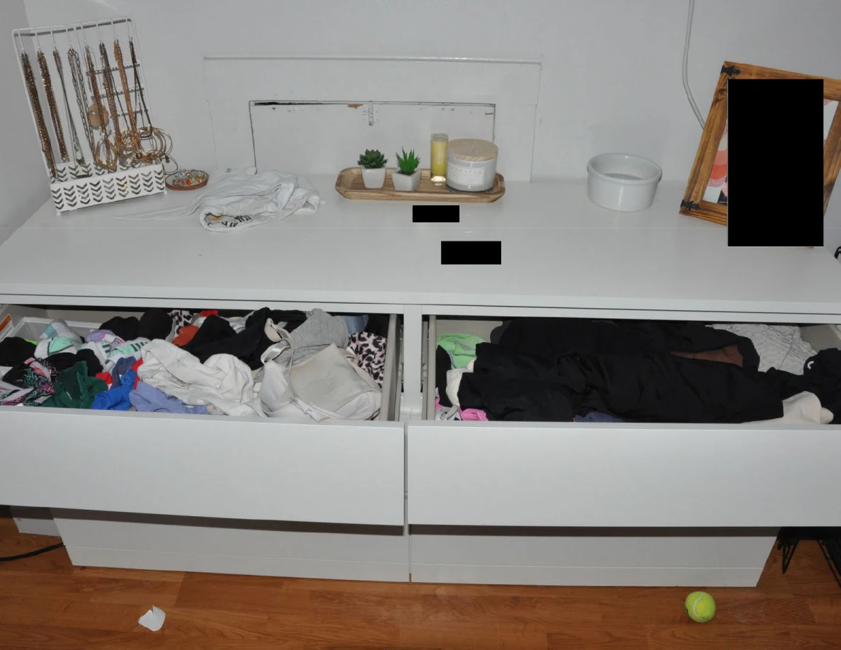 Open dresser drawers filled with assorted clothing below jewelry and small plants.