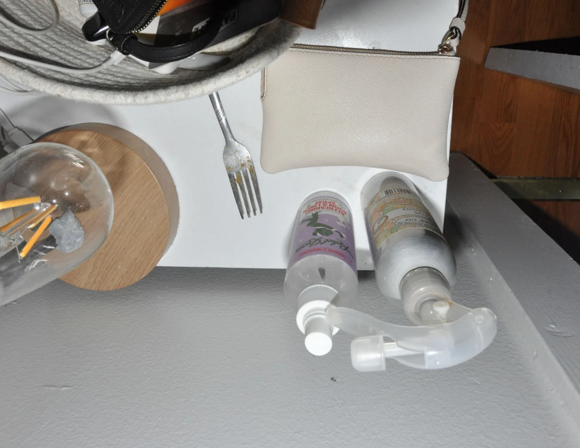 Pale wristlet, fork, spray bottle and pump bottle beside a lamp and woven basket.