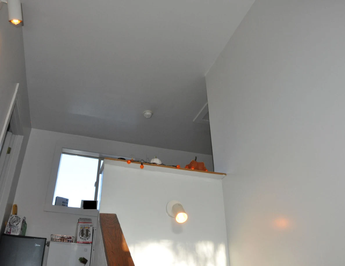 Upper stairwell wall and ceiling with lights, window and decorations along a ledge.
