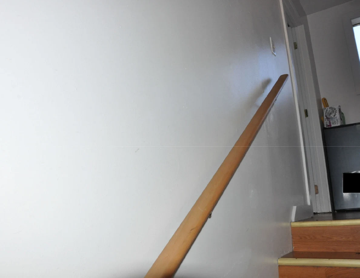 Wooden handrail rising along a pale stairwell wall.