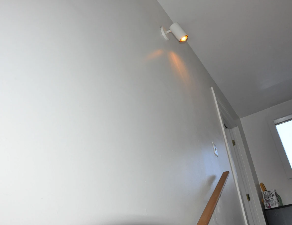 Upper stairwell wall with a lit wall fixture above the handrail.