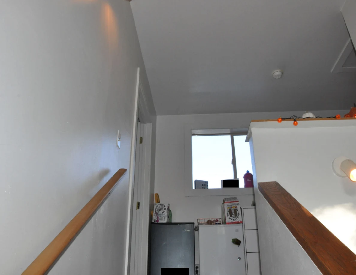 Stairway toward a landing with compact refrigerators, window and decorated half-wall.