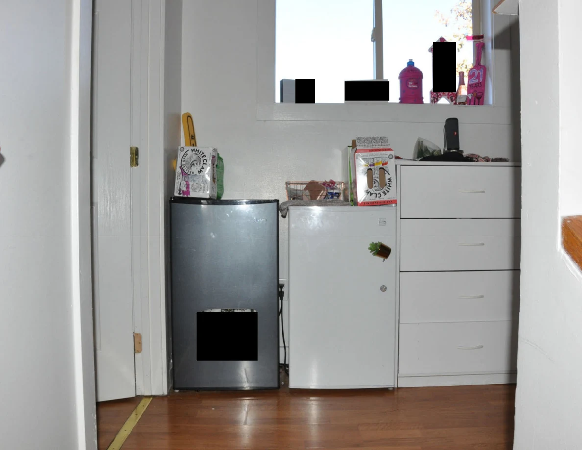Compact refrigerators and white drawers beneath a window with containers on the sill.