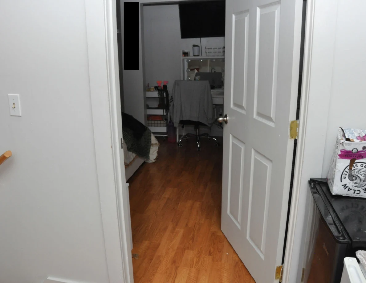 Open bedroom doorway facing a vanity, chair and wall television.