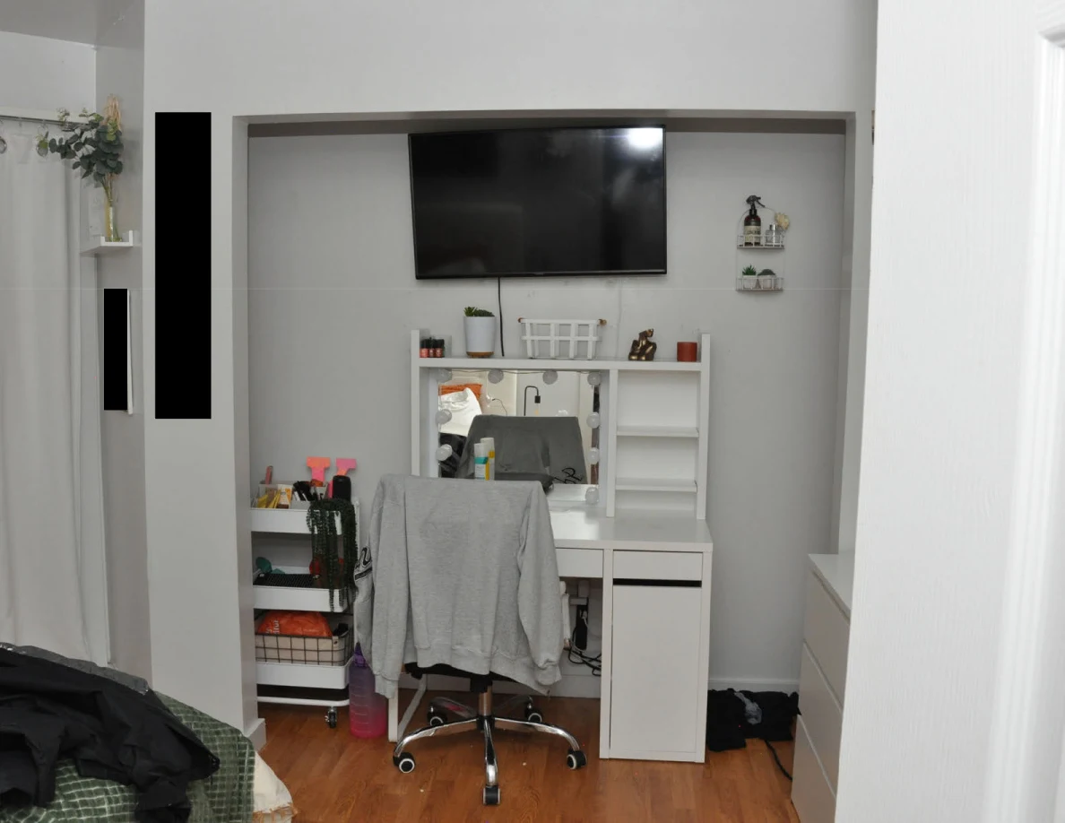 Bedroom vanity with chair and wall television beside small shelves and redacted areas.