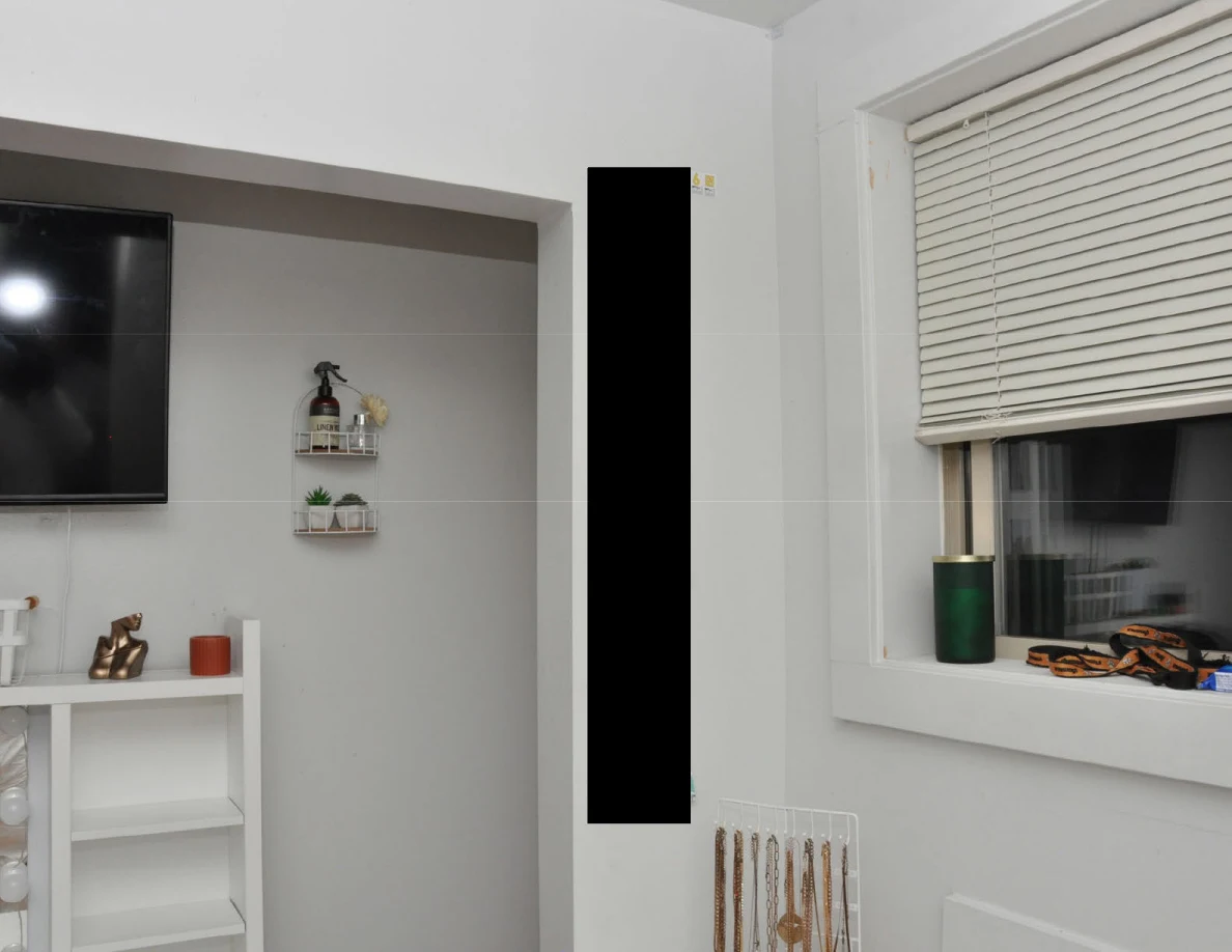 Television edge and small wall baskets beside a window with blinds and green tumbler.