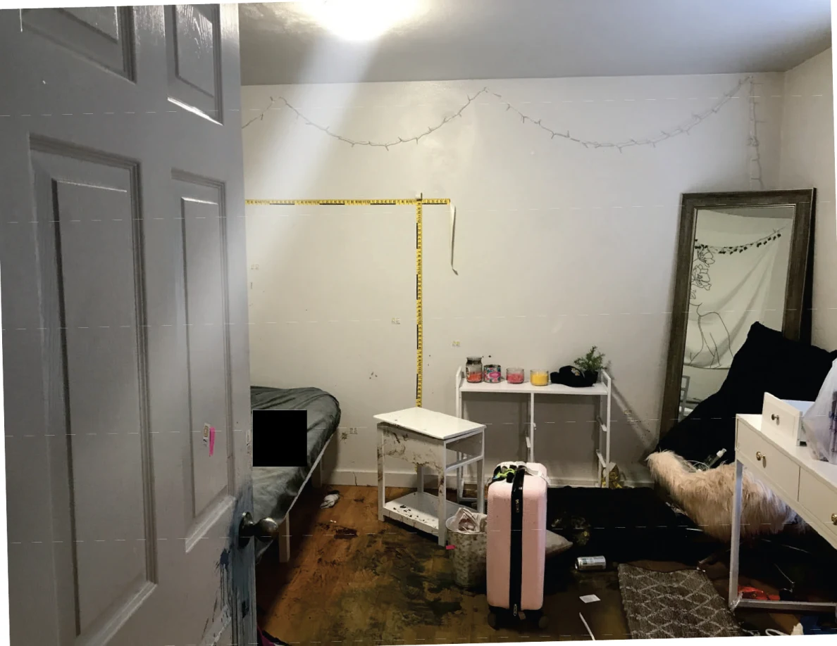 Bedroom with yellow measurement tape on walls, a bed, mirror, white furniture and pink suitcase; part of the bed is redacted.