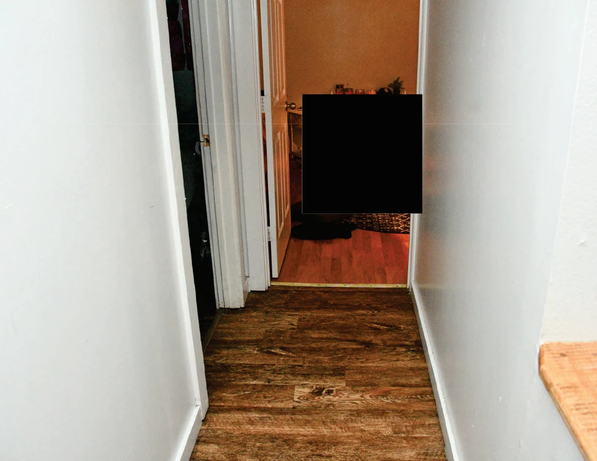 Narrow hallway toward an orange-lit room with a large black redaction at the far end.