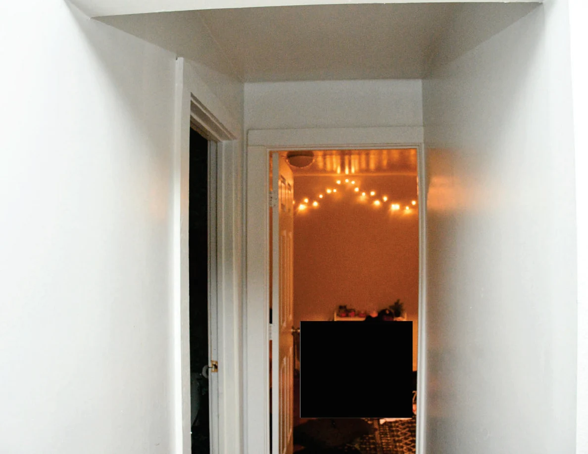 Upper hallway view toward string lights in a partly redacted room.