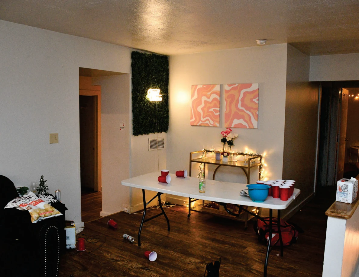 Living room with a white cup-pong table, red cups and blue bowl beneath pink artwork and string-lit console table.
