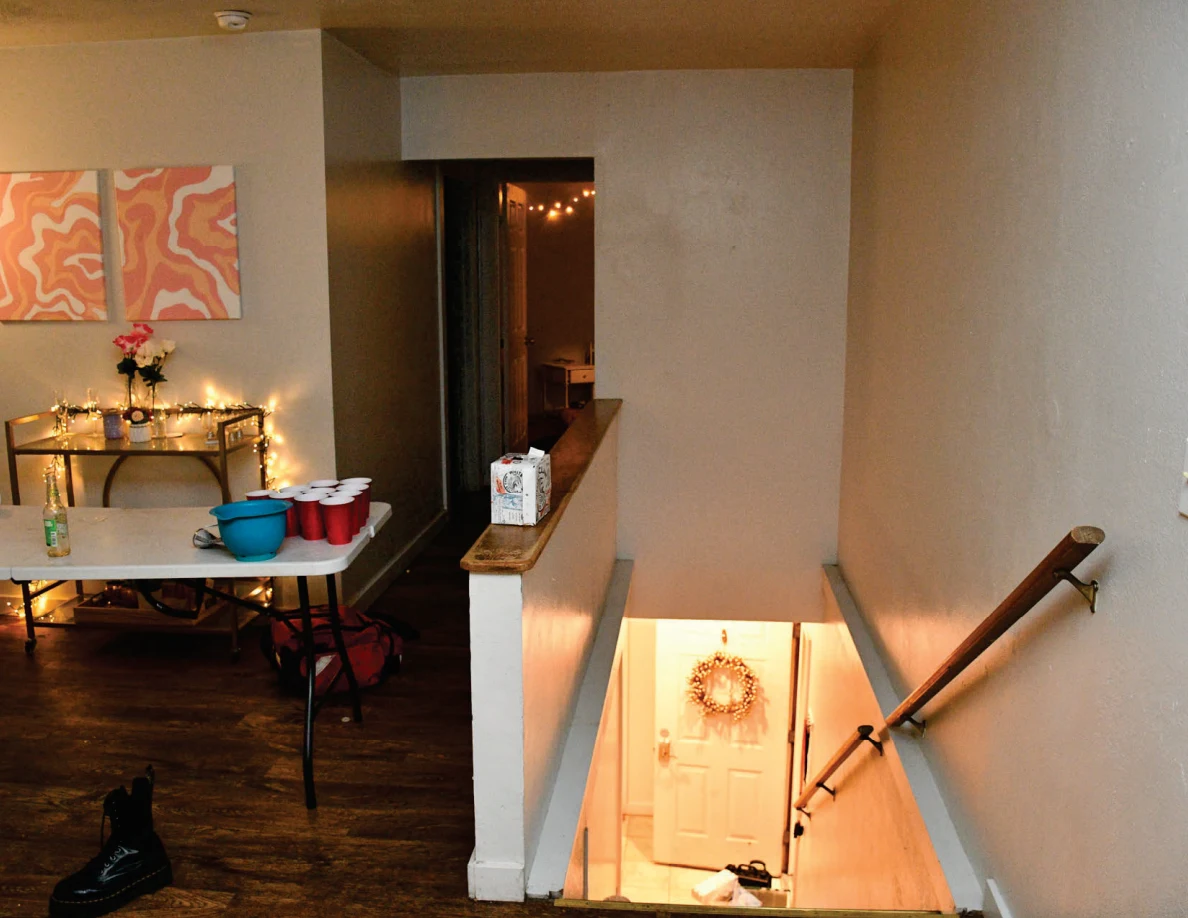 Cup-pong table beside an open stairwell with wooden handrail and a door at the bottom.