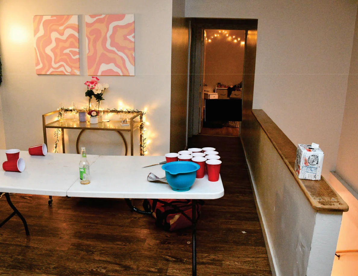 White cup-pong table with grouped red cups, bottle and blue bowl beside a decorated console.