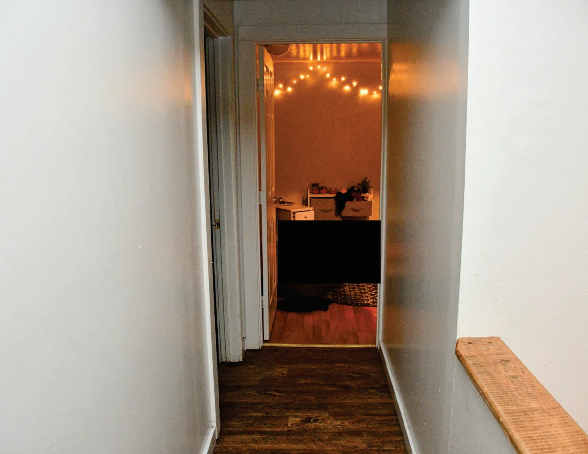Hallway leading to an orange-lit room with string lights and redacted areas.