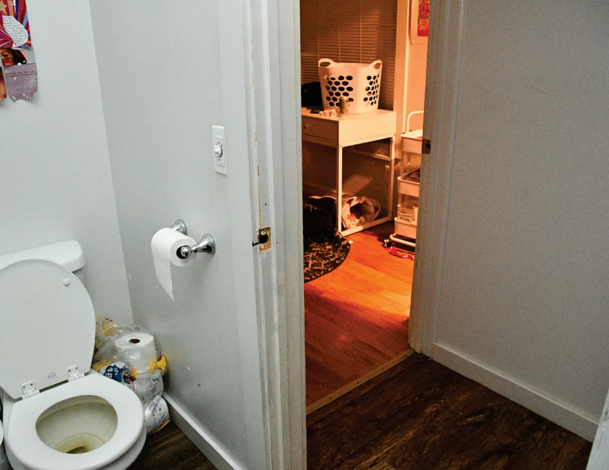 Bathroom toilet beside an open doorway into a room with a laundry basket on a white table.