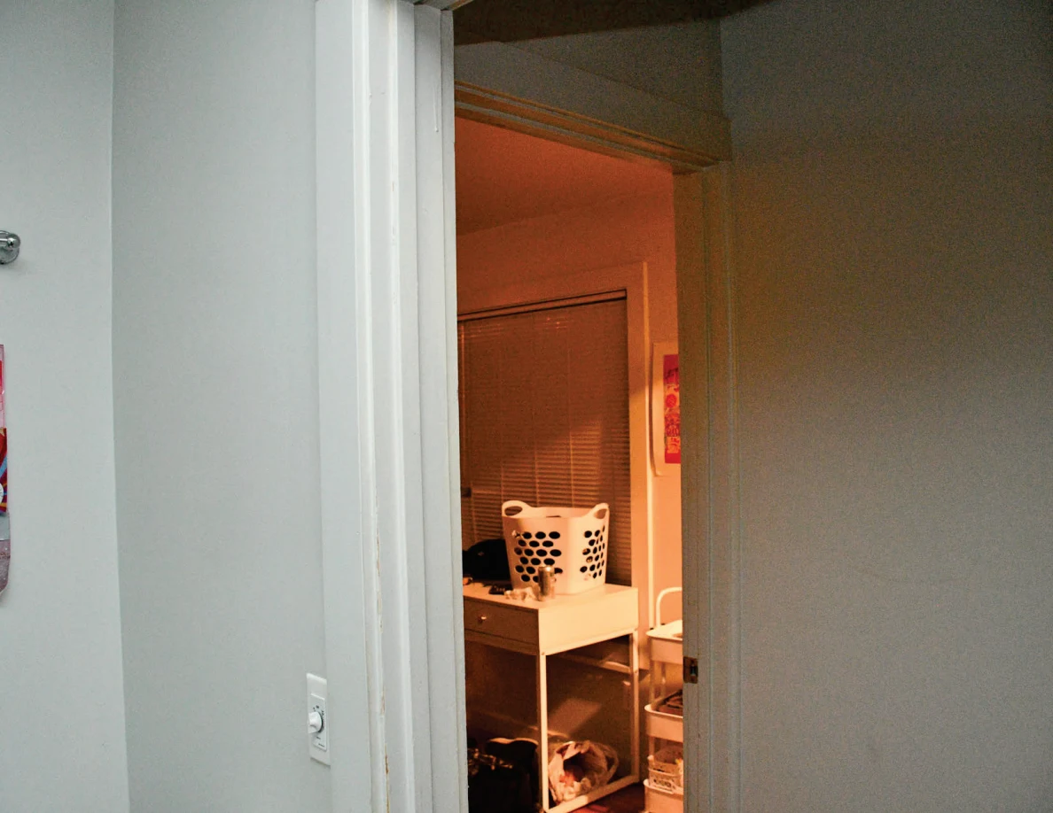 Upper bathroom doorway looking toward a laundry basket and window blinds.