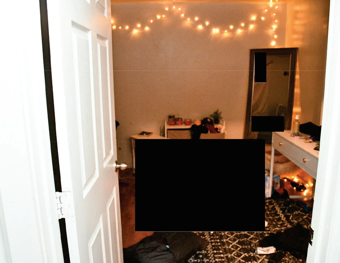 Open bedroom door facing string lights, a tall mirror and white furniture with large redactions.