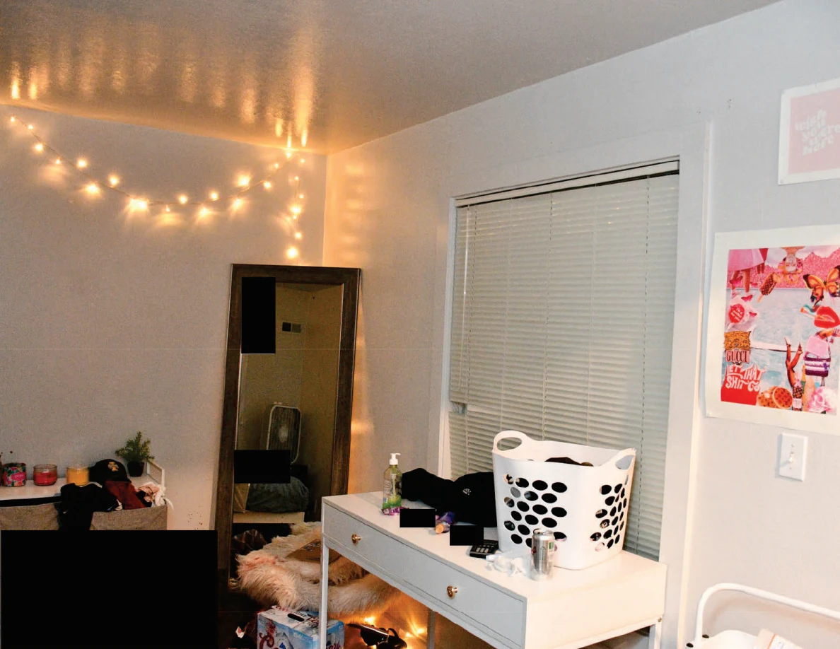 Window blinds above a white desk and laundry basket beside a tall mirror and pink wall art.