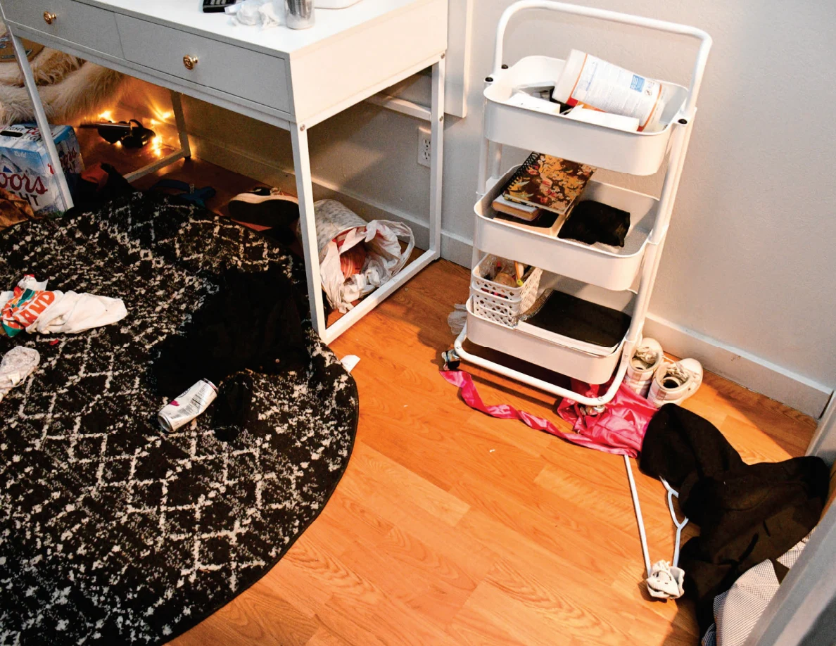 Rolling cart beside a white desk with scattered clothing and a dark patterned round rug on the floor.